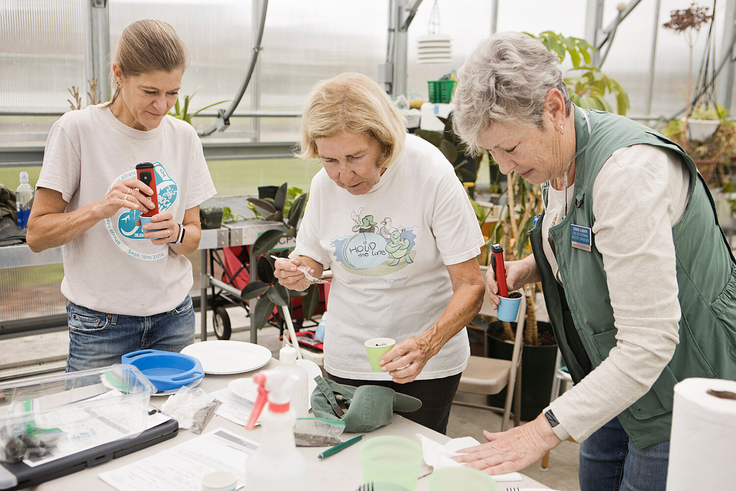 Melinda Viera, Barbara Jones, and Ednor Larson mix and test soil inside the Veterans Home greenhouse, Saturday morning.