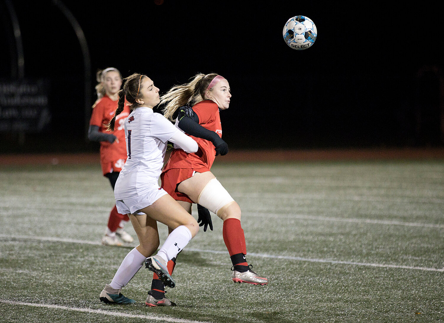 Lily Ferreira is pressured closely from behind while heading a pass toward a teammate.