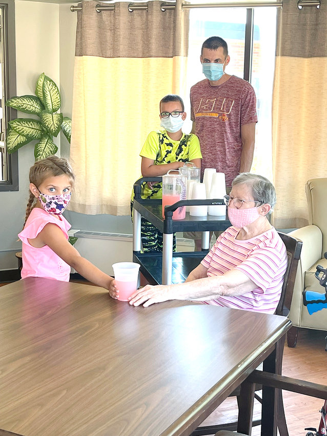 Karlee Radtke hands a fresh glass of pink lemonade to Good Samaritan Society Resident Betty Smith, who was ready and waiting dressed in pink. Karlee and her older brother, Huxley, center, had wanted to set up a lemonade stand in the recent heat wave, but their parents said it would be better to serve lemonade to the residents. Kirk Radtke, right, was named Champion in Volunteering for Good Samaritan Center.  Photo by Amy H. Peterson