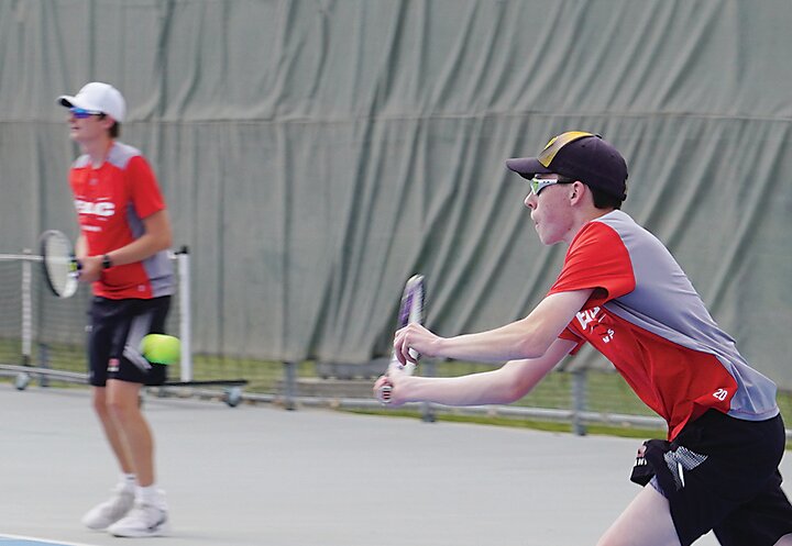 At left, Estherville Lincoln Central&rsquo;s Brenden Lundgren hits a return during his singles match while teammate Matt Valen waits for a serve in the neighboring court.
