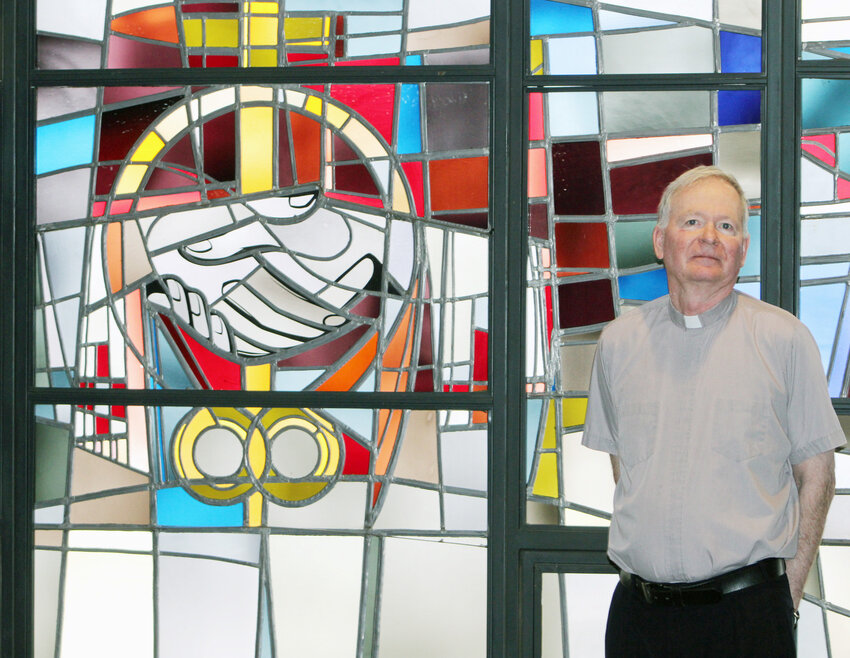 Father Paul Kelly stands in front of the bank of stained glass windows on the east side of St. Patrick’s Catholic church. The windows will be restored over the summer.