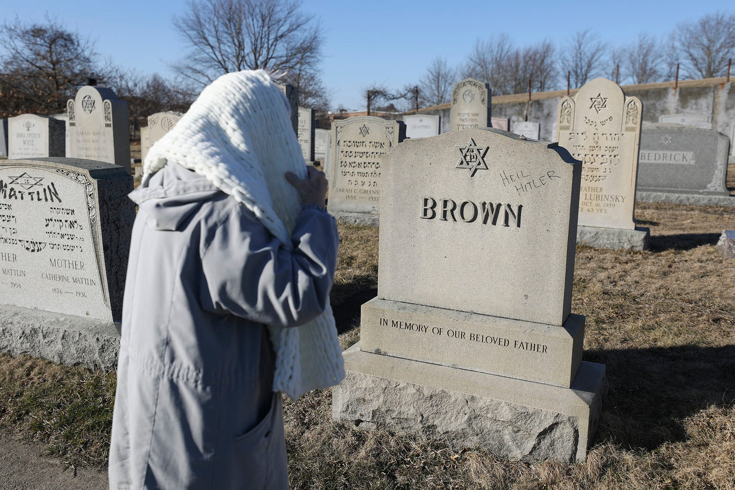 A woman stops to look at a vandalized  grave stone in the cemetery.