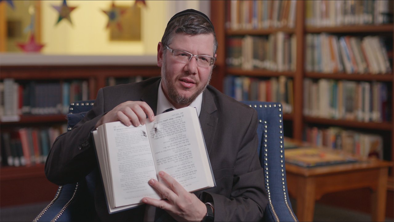 In “Viral: Antisemitism in Four Mutations,” Rabbi Elisar Admon shows the hole where a bullet pierced his prayer book during the Tree of Life Synagogue shooting in Pittsburgh. "It went right through the word for God," he said.