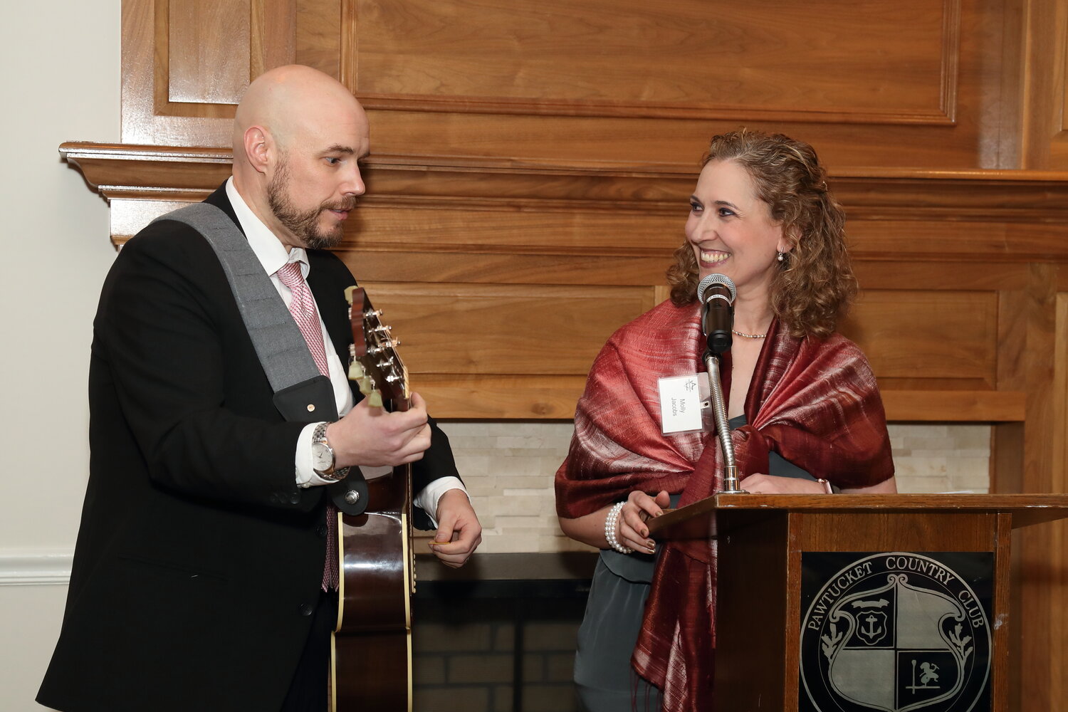 Congregation Agugas Achim president Molly Jacobs (right) sings a Jewish camp song to conclude her remarks, accompanied by member Ken Freeman on guitar.