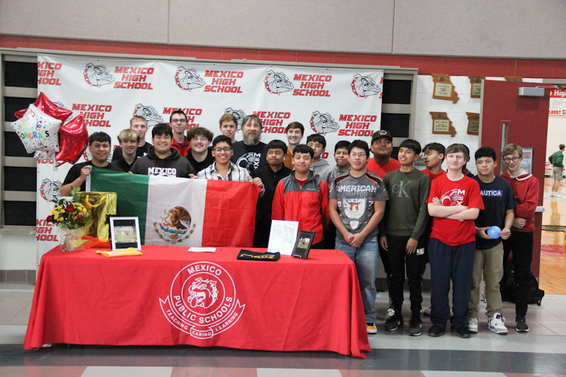 Mexico senior Fernando Guzman (third from left in front row) holds up the Mexican flag on Monday while being surrounded by his teammates at his college signing with Kansas NJCAA school Hesston College.