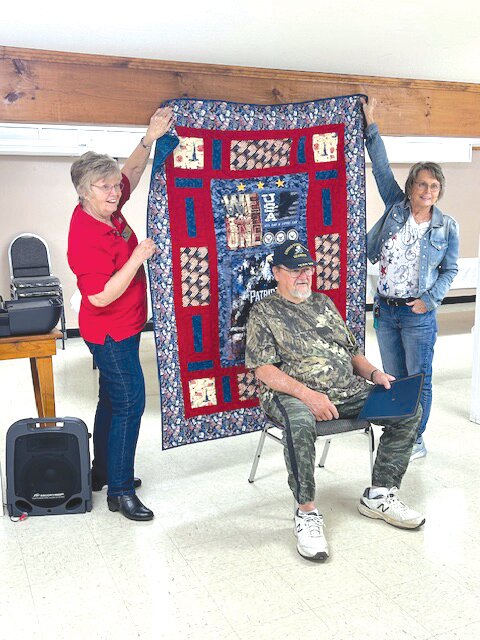 Navy Veteran Jim Utterback receives Quilt of Valor displayed by Joyce Lowry and Donna Hoffman.