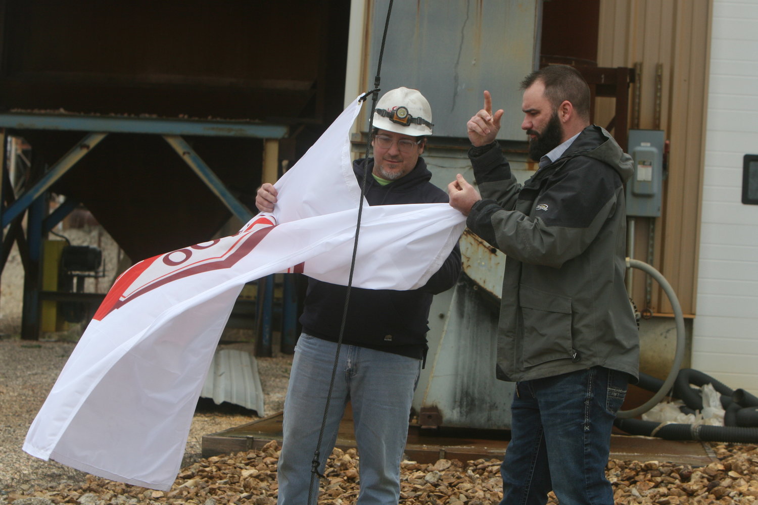 Eddie Rose, assistant manager of the Christy Minerals plant in High Hill, and military representative Steve Lomelino work on raising the Christy Minerals’ 100th anniversary flag on April 20.