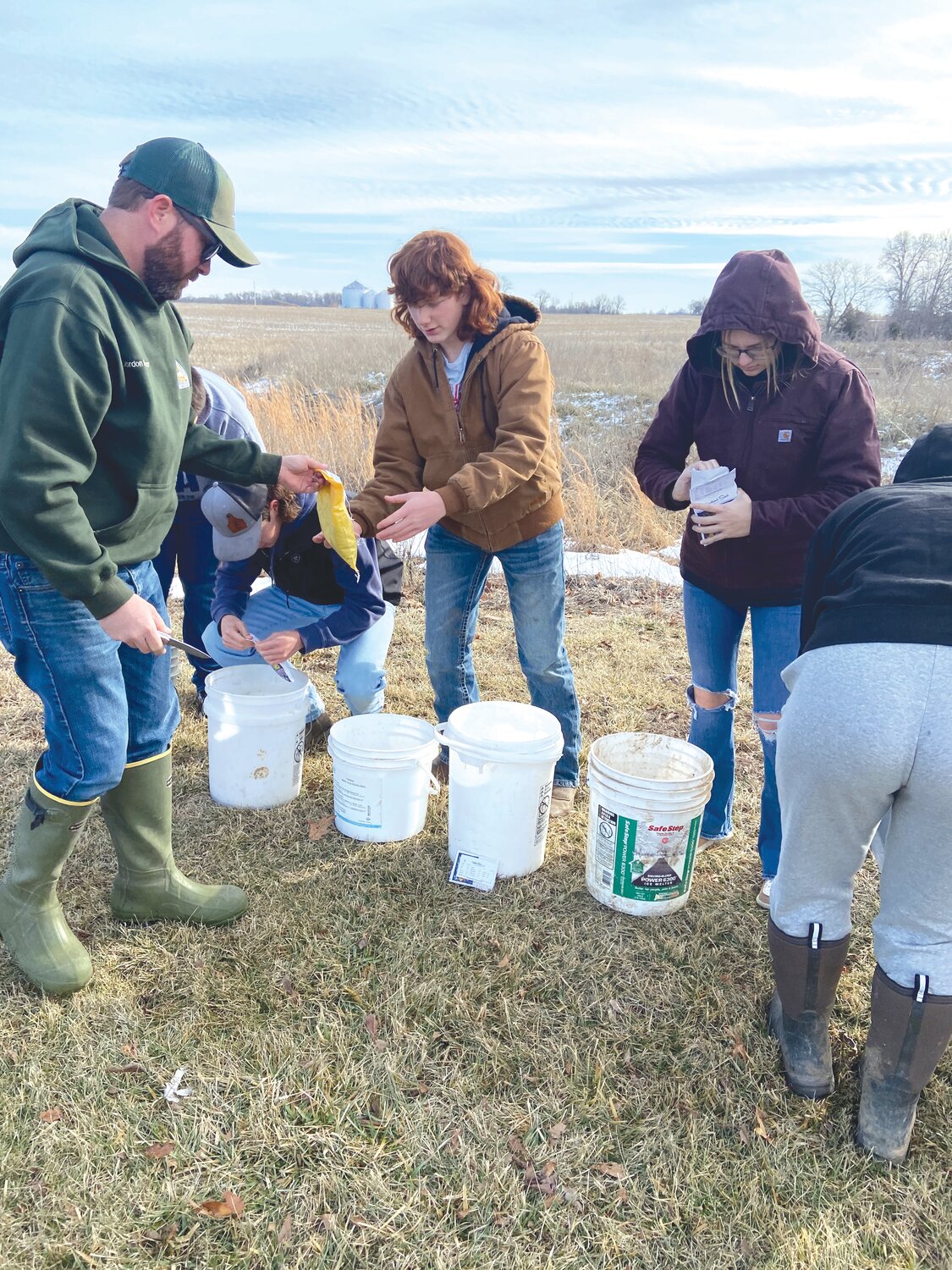 Jordan Beshears of the Missouri Department of Conservation, left, hands out seeds to junior Brayden Harris while working on the prairie project. On the right is senior Presley Schluss.
