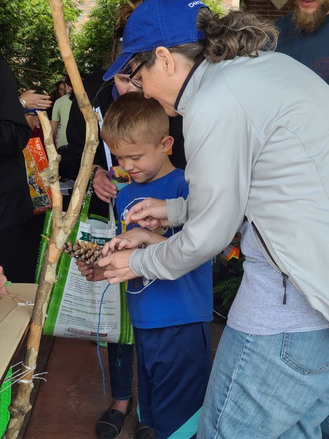 Sperry-Galligar Audubon member Megan Corrigan, right, helps Dylan Manion, left, tie a piece of yarn to a pinecone that will be made into a birdfeeder during the Earth Day Celebration on Saturday.