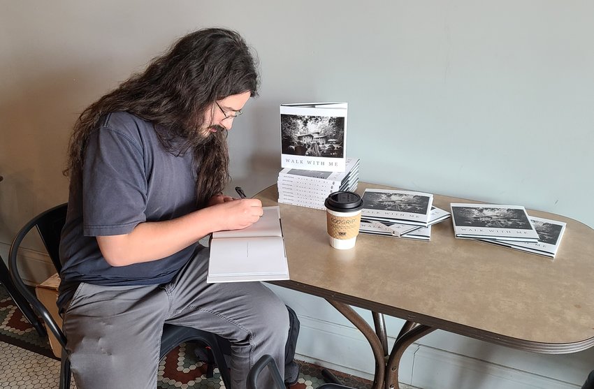 Photographer Seth Potter signs copies of his first published photography book, titled &ldquo;Walk with Me,&rdquo; during the reception for his exhibit at Root Coffeehouse on Tuesday. Potter said the inspiration for the title was due to the fact he walked hundreds of miles to accumulate the 50 photos in his book. &ldquo;I&rsquo;ve worn out several pairs of shoes,&rdquo; he said.