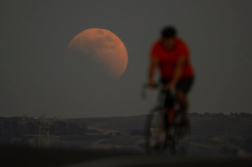 A lunar eclipse is seen behind a cyclist during the first blood moon of the year, in Irwindale, Calif., Sunday, May 15, 2022. (AP Photo/Ringo H.W. Chiu)
