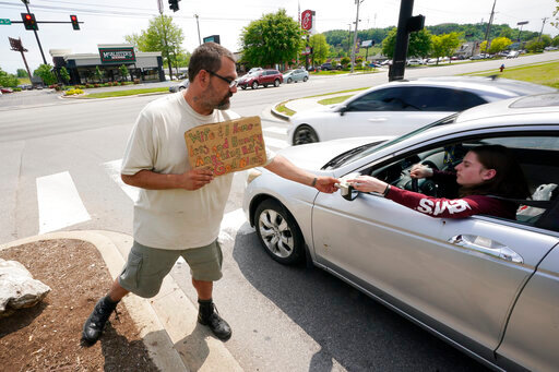 Adam Atnip, who is homeless and lives in his car, accepts money from a driver as he panhandles on May 10, 2022, in Cookeville, Tenn. Tennessee is about to become the first U.S. state to make it a felony to camp on local public property such as parks. (AP Photo/Mark Humphrey)