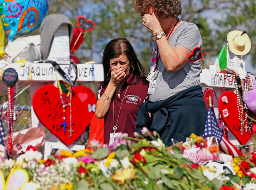 FILE - Marjory Stoneman Douglas High School administrative employees Margarita LaSalle, left, and JoEllen Berman, walk along the hill near the school lined with 17 crosses to honor the students and teachers killed on Valentine's Day, as teachers and staff returned to the school, Feb. 23, 2018, in Parkland, Fla. There have been dozens of shootings and other attacks in U.S. schools and colleges over the years, but until the massacre at Colorado's Columbine High School in 1999, the number of dead tended to be in the single digits. Since then, the number of shootings that included schools and killed 10 or more people has mounted. (Charles Trainor Jr/Miami Herald via AP, File)