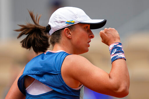 Poland's Iga Swiatek, who plays with a ribbon in the colors of the Ukraine flag on her cap, clenches her fist after scoring a point against Montenegro's Danka Kovinic during their third round match at the French Open tennis tournament in Roland Garros stadium in Paris, France, Saturday, May 28, 2022. (AP Photo/Michel Euler)