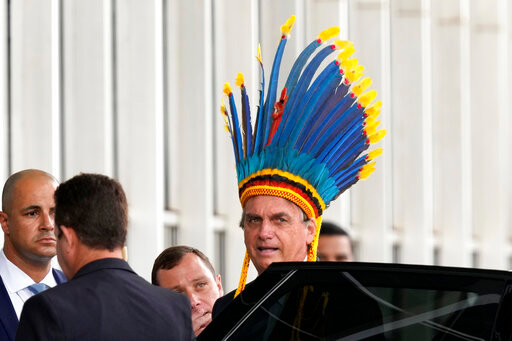 FILE - Brazil's President Jair Bolsonaro, wearing a traditional Paresi Indigenous headdress, leaves after participating in a ceremony where he was decorated with the Medal of Indigenous merit, at the Ministry of Justice, in Brasilia, Brazil, March 18, 2022. The accolade scandalized environmentalists, human rights activists and Indigenous groups who see the president&rsquo;s push for development within Indigenous territories as profoundly damaging. (AP Photo/Eraldo Peres, File)