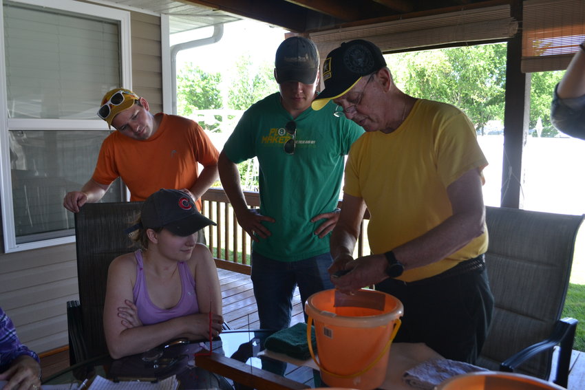 From left, Pittsburg State University students Haley Price, Luke Headings, and Jeremiah Casner observe Master Bird Bander Tim Mangan as he shows them how to properly hold a purple martin fledgling&nbsp;and where to attach the band at his residence on Tuesday.