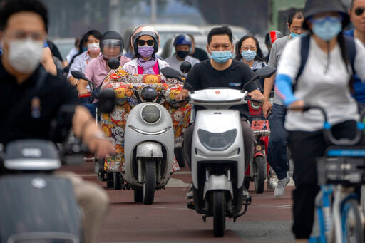 Commuters wearing face masks ride across an intersection in the central business district in Beijing, Friday, June 17, 2022. (AP Photo/Mark Schiefelbein)