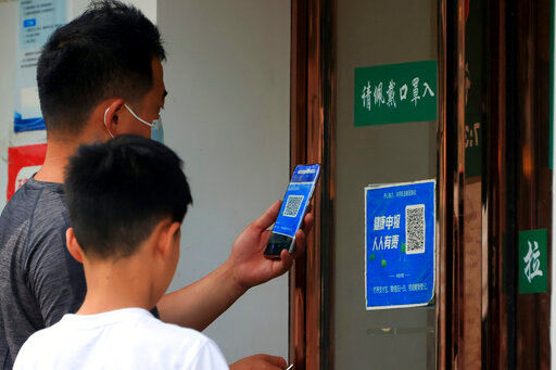 A man wearing a face mask scans a QR code for a health monitoring app to enter a shop in Zhengzhou in central China's Henan Province, Friday, June 17, 2022. Angry bank customers who traveled to a city in central China attempting to retrieve their savings from troubled rural banks were stopped in their tracks by a common technology: a QR code. (Chinatopix via AP)
