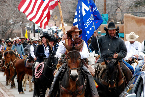 FILE - In this March 12, 2019 file photo, advocates for gun rights in New Mexico including rural ranchers joined with a interstate group called Cowboys for Trump, approach the New Mexico state Capitol in Santa Fe on horseback. Behind the raw public frustration and anger over election security that has played out this week in New Mexico was a hint of something deeper -- a growing divide between the state&rsquo;s Democratic power structure and conservative rural residents who feel their way of life is under attack.   (AP Photo/Morgan Lee, File)