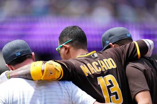 San Diego Padres' Manny Machado, center, is helped off the field after injuring his ankle while running out a ground ball hit to Colorado Rockies starting pitcher Antonio Senzatela in the first inning of a baseball game Sunday, June 19, 2022, in Denver. Machado was called out on the play. (AP Photo/David Zalubowski)