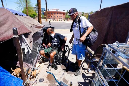 &quot;Cueball&quot;, left, talks about his dog Lindsay with neighbor Terry Reed, right, at their tents Friday, May 20, 2022, in Phoenix. Hundreds of homeless people die in the streets each year from the heat, in cities around the U.S. and the world. The ranks of homeless have swelled after the pandemic and temperatures fueled by climate change soar. (AP Photo/Ross D. Franklin)