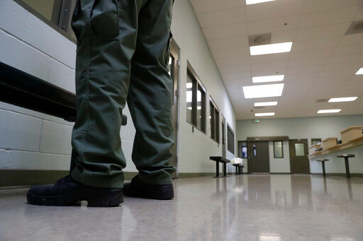 FILE - In this Aug. 28, 2019, photo, a guard stands in the intake area at the Adelanto ICE Processing Center in Adelanto, Calif. In a wind-whipped California desert town, a sprawling facility can house nearly 2,000 immigrant detainees facing the prospect of deportation. These days, however, the privately-run detention center in Adelanto is nearly empty. (AP Photo/Chris Carlson, File)
