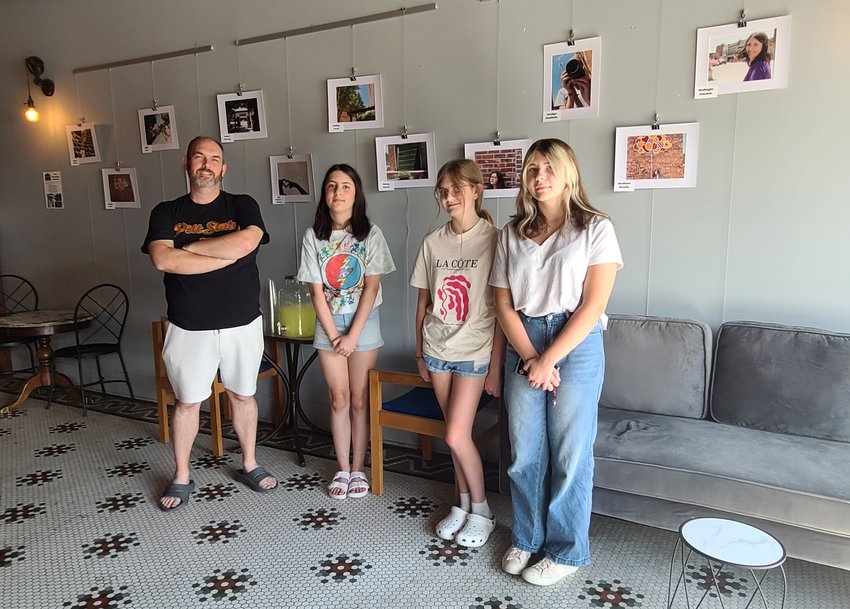 From left, Rion Huffman stands with his students, Izzy DeLuna-Vickery, Caylee Gudde, and Clover Murray at the reception for the Youth Photography Workshop in front of the class&rsquo;s images at Root Coffeehouse on Tuesday.