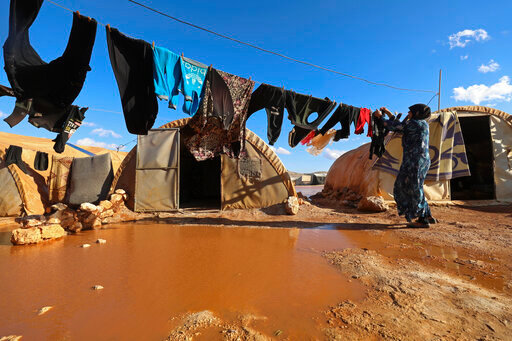 FILE - A woman hangs laundry in a flooded refugee camp in Idlib province, Syria, Dec. 21, 2021. Syrians in the last major rebel stronghold in the war-ton country are living in fear of the effects of Russia closing down the only border crossing into the northwestern province of Idlib. Aid agencies warn that if Russia vetoes the resolution that would maintain two border crossing points from Turkey to deliver humanitarian aid, food would be depleted in Idlib and surrounding areas by September, 2022, putting the lives of some 4.1 million people, at risk. (AP Photo/Ghaith Alsayed, File)