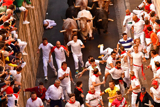 People run through the street with fighting bulls at the San Fermin Festival in Pamplona, northern Spain, Friday, July 8, 2022. Revellers from around the world flock to the city every year for nine days of uninterrupted partying in Pamplona's famed running of the bulls festival which was suspended for the past two years because of the coronavirus pandemic. (AP Photo/Alvaro Barrientos)