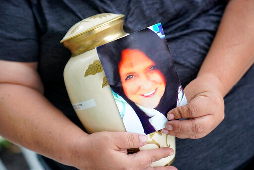 Kelly Titchenell sits on her porch in Mather, Pa., holding a photo of her mother Diania Kronk, and an urn containing her mother's ashes, Thursday, July 7, 2022. A Greene County, Pa., detective last week filed charges against 911 operator Leon &ldquo;Lee&rdquo; Price, 50, of Waynesburg, in the July 2020 death of Diania Kronk, 54, based on Price's reluctance to dispatch help without getting more assurance that Kronk would actually go to the hospital. (AP Photo/Gene J. Puskar)