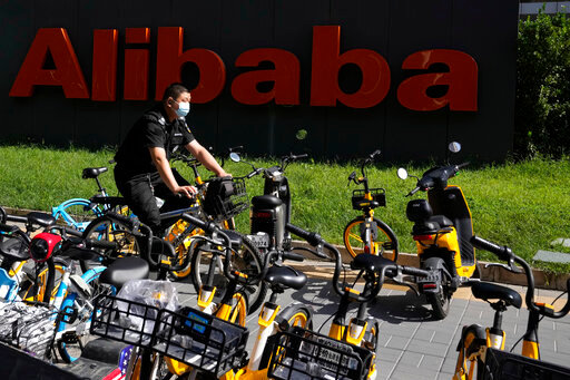 A Chinese security guard rides past the logo for Chinese tech firm Alibaba in Beijing, China on Aug. 24, 2021. Shares of Chinese technology firms Alibaba and Tencent plunged Monday, July 11, 2022, a day after Chinese regulators fined their subsidiaries for not disclosing transactions and failing to comply with anti-monopoly rules. (AP Photo/Ng Han Guan)