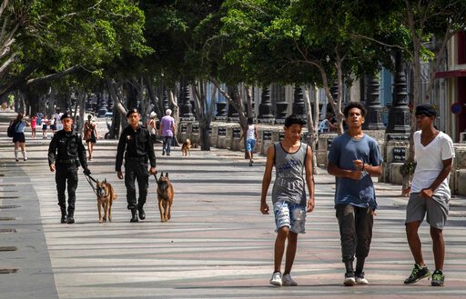 People walk at the Paseo del Prado while members of the police patrol in Havana, Cuba, Monday, July 11, 2022. A year after the largest protests in decades shook Cuba's single-party government, the economic and political factors that caused them largely remain. (AP Photo/Ramon Espinosa)