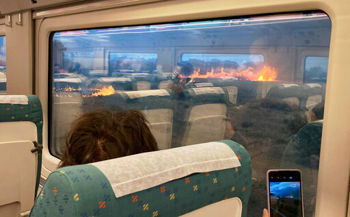 Passengers take photos at a wildfire while traveling on a train in Zamora, Spain, Monday, July 18, 2022. When Francisco Seoane's train unexpectedly stopped in Spanish countryside that was being engulfed by a wildfire, he and other passengers got a fright when they looked out at flames encroaching on both sides of the track. The Spaniard told The Associated Press it was scary to see how quickly the fire spread. Video of the unscheduled &mdash; and unnerving &mdash; stop shows about a dozen passengers in Seoane's railcar appearing alarmed as they look out of the windows Monday. (AP Photo/Francisco Seoane Perez)