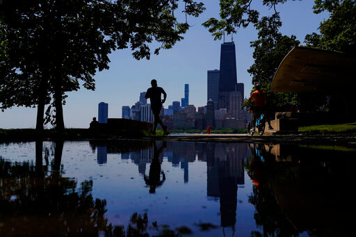 A runner jogs along a path on the shore of Lake Michigan as the downtown skyline is seen in the background, Tuesday, July 19, 2022, in Chicago. (AP Photo/Kiichiro Sato)