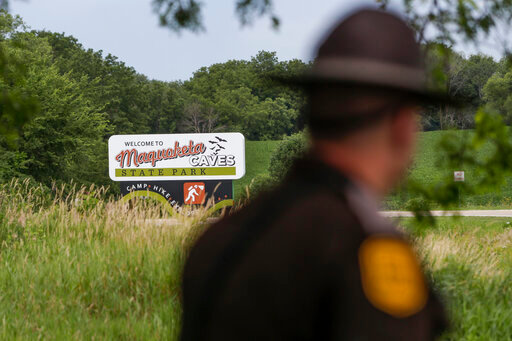An Iowa State Patrolman walks past a Maquoketa Caves State Park sign as police investigate a shooting that left several people dead, Friday, July 22, 2022, in Maquoketa, Iowa. The campground was evacuated in the wake of the shooting. (Nikos Frazier/Quad City Times via AP)