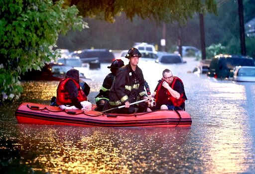 Steven Bertke and his dog Roscoe are taken to dry land by St. Louis firefighters who used a boat to rescue people from their flooded homes on Hermitage Avenue in St. Louis on Tuesday, July 26, 2022. (David Carson/St. Louis Post-Dispatch via AP)