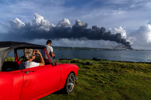 People watch a plume of smoke rise from the Matanzas supertanker base where a deadly fire started during a thunderstorm the night before in Matanzas, Cuba, Sunday, Aug. 7, 2022. The blaze forced officials to evacuate more than 4,900 people, has killed two firefighters, injured 130 people and destroyed four of the facility's eight tanks. (AP Photo/Ramon Espinosa)