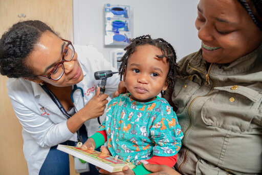 In this 2019 photo provided by Zero to Three, a pediatrician checks on a child as their mother looks on at Children&rsquo;s National Hospital in Washington.   Zero to Three&rsquo;s HealthySteps program aims to help children meet important milestones by placing early-childhood-development specialists in pediatric primary-care practices.  (Courtesy of Zero to Three via AP)