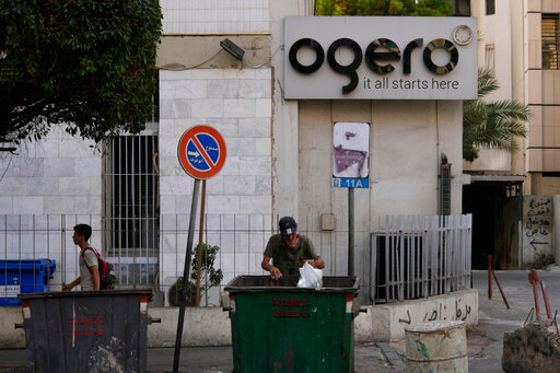 A man scavenges in the garbage next to a building of the state-owned telecom and internet company, Ogero, in Beirut, Lebanon, Wednesday, Aug. 31, 2022. Internet shutdowns rippled through cash-strapped Lebanon on Tuesday after employees of Ogero went on strike, demanding higher wages. (AP Photo/Hassan Ammar)