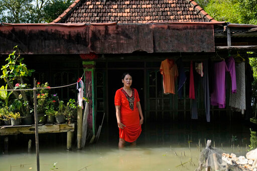 Zuriah stands outside her flooded home in Mondoliko, Central Java, Indonesia, Monday, Aug. 1, 2022. Unable to afford to move to a new home, Zuriah continues to live in the house even as nearly all of her neighbors move away. (AP Photo/Dita Alangkara)