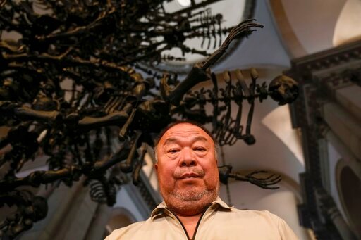 Chinese artist Ai Weiwei poses in front of his unveil glass body of work 'La Commedia Umana' a huge hanging glass sculpture otherwise referred to as a 'chandelier' at the San Giorgio deconsecrated church in Venice, Italy, Friday, Aug. 26, 2022. Chinese artist Ai Weiwei lampoons the surveillance culture and social media with his first ever glass sculpture, made on the Venetian island of Murano, that stands as a warning to the world: &quot;Memento Mori,'' or Latin for &quot;Remember You Must Die.&quot; (AP Photo/Luca Bruno)