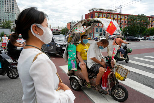 FILE- A man and a child wearing masks sit in an electric tricycle with a Chinese national flag in Beijing, on Aug. 15, 2022. A Chinese think tank issued a rare public disagreement Monday, Aug. 29, 2022, with the ruling Communist Party&rsquo;s severe &ldquo;zero COVID&rdquo; policy, saying curbs that shut down cities and disrupt trade, travel and industry must change to prevent an &ldquo;economic stall.&rdquo;(AP Photo/Ng Han Guan, File)