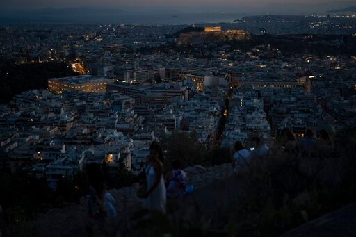 FILE - People admire the view of the city of Athens with the Greek Parliament on the left and the ancient Acropolis hill on the right, on Aug. 10 , 2022. Greece's government on Wednesday, Sept. 7, 2022 announced a carrot-and-stick drive to cut public sector energy use by 10% this year, linking compliance to funding and urging state employees to switch off lights and appliances when leaving the office. (AP Photo/Petros Giannakouris, File)