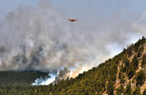 FILE - A firefighting plane flies over plumes of smoke near Las Vegas, N.M. on May 4, 2022. The U.S. government is resuming prescribed burning of National Forest lands across the nation to clear brush and small trees after a three-month pause to review and respond to climate change and risks of runaway wildfires. U.S. Forest Service Chief Randy Moore said newly prescribed burns will require same-day authorization to keep pace with weather and ground conditions. (AP Photo/Thomas Peipert, File)