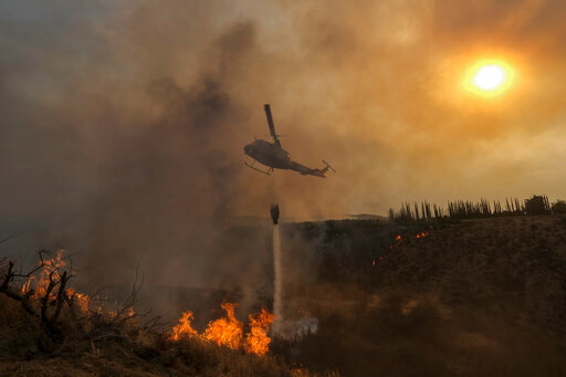 FILE - A helicopter drops water on the Fairview Fire burning on a hillside Thursday, Sept. 8, 2022, near Hemet, Calif. Scientists say a warming planet will lead to hotter, longer and more wildfire-plagued heat waves. (AP Photo/Ringo H.W. Chiu, File)
