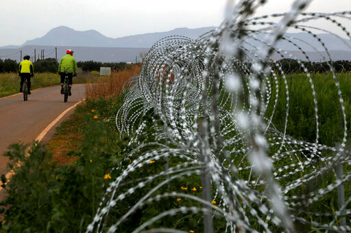 FILE - Two men cycle along a row of razor wire along the southern side of a U.N buffer zone that cuts across the ethnically divided Cyprus, during sunset near village of Astromeritis, on March 9, 2021. Cyprus is seeking help from the United Nations to stem an &ldquo;avalanche&rdquo; of migrants who make their way from the ethnically divided island&rsquo;s breakaway north across a UN controlled buffer zone to seek asylum in numbers that authorities cannot cope with, the Cypriot interior minister said Monday Sept. 26, 2022. (AP Photo/Petros Karadjias, File)