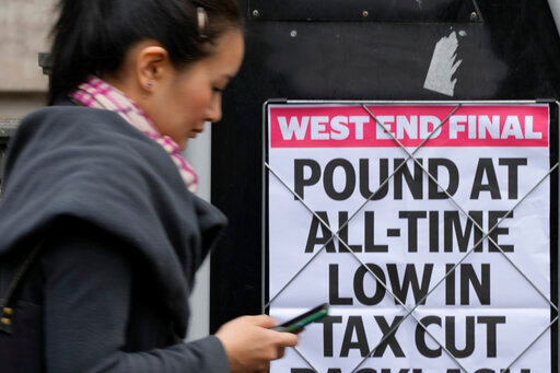 A woman walks past a headline posted on a wall in London, Tuesday, Sept. 27, 2022. The British pound has stabilized in Asian trading after plunging to a record low, as the Bank of England and the British government try to soothe markets nervous about a volatile U.K. economy. The instability is having real-world impacts, with several British mortgage lenders withdrawing deals amid concern that interest rates may soon rise sharply. (AP Photo/Frank Augstein)
