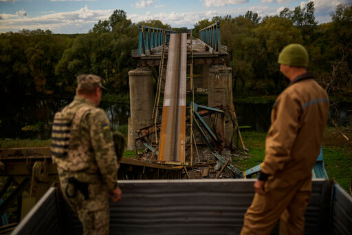 Ukrainian soldiers remove metal structure pieces as they work on a bridge damaged during fighting with Russian troops in Izium, Ukraine, Monday, Oct. 3, 2022. A series of embarrassing military losses for Moscow in recent weeks has presented a growing challenge for prominent hosts of Russian news and political talk shows scrambling to find ways to paint Kyiv's gains in a way that is still favorable to the Kremlin. (AP Photo/Francisco Seco)