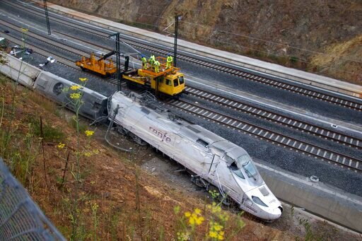 FILE - Rail workers are seen next to derailed cars at the site of a train accident in Santiago de Compostela, Spain, on July 25, 2013. A trial has begun in Spain on Wednesday Oct. 5, 2022 for the 2013 train accident that killed 80 passengers and injured 145 others. Prosecutors are seeking four-year prison sentences for the train driver and for a former security director at the rail infrastructure company, ADIF after the long-distance train derailed and crashed against a concrete wall while traveling over the speed limit. (AP Photo/Lalo Villar, File)