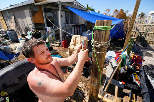 Joe Kuczko puts up a tarp next to his mobile home, Thursday, Oct. 6, 2022, in Pine Island, Fla.,  in the aftermath of Hurricane Ian, (AP Photo/Wilfredo Lee)